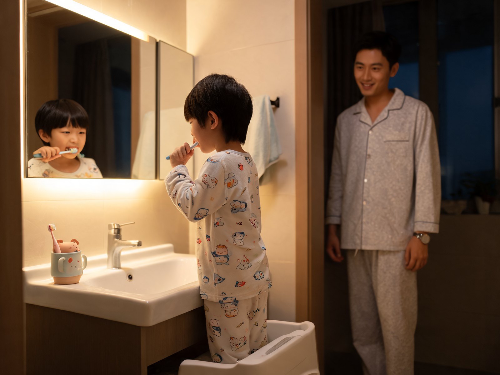 Child brushing teeth at a bathroom sink with a parent nearby