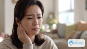 Woman gently holding the side of her jaw, a common sign of jaw joint or muscle pain