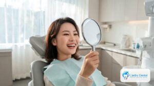 Smiling woman in a Reseda dental office chair checking her brighter teeth in a hand mirror after professional whitening